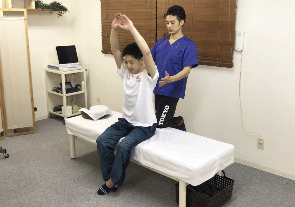 腕を上げる男性アスリートと肩甲骨の動きを確認する施術者