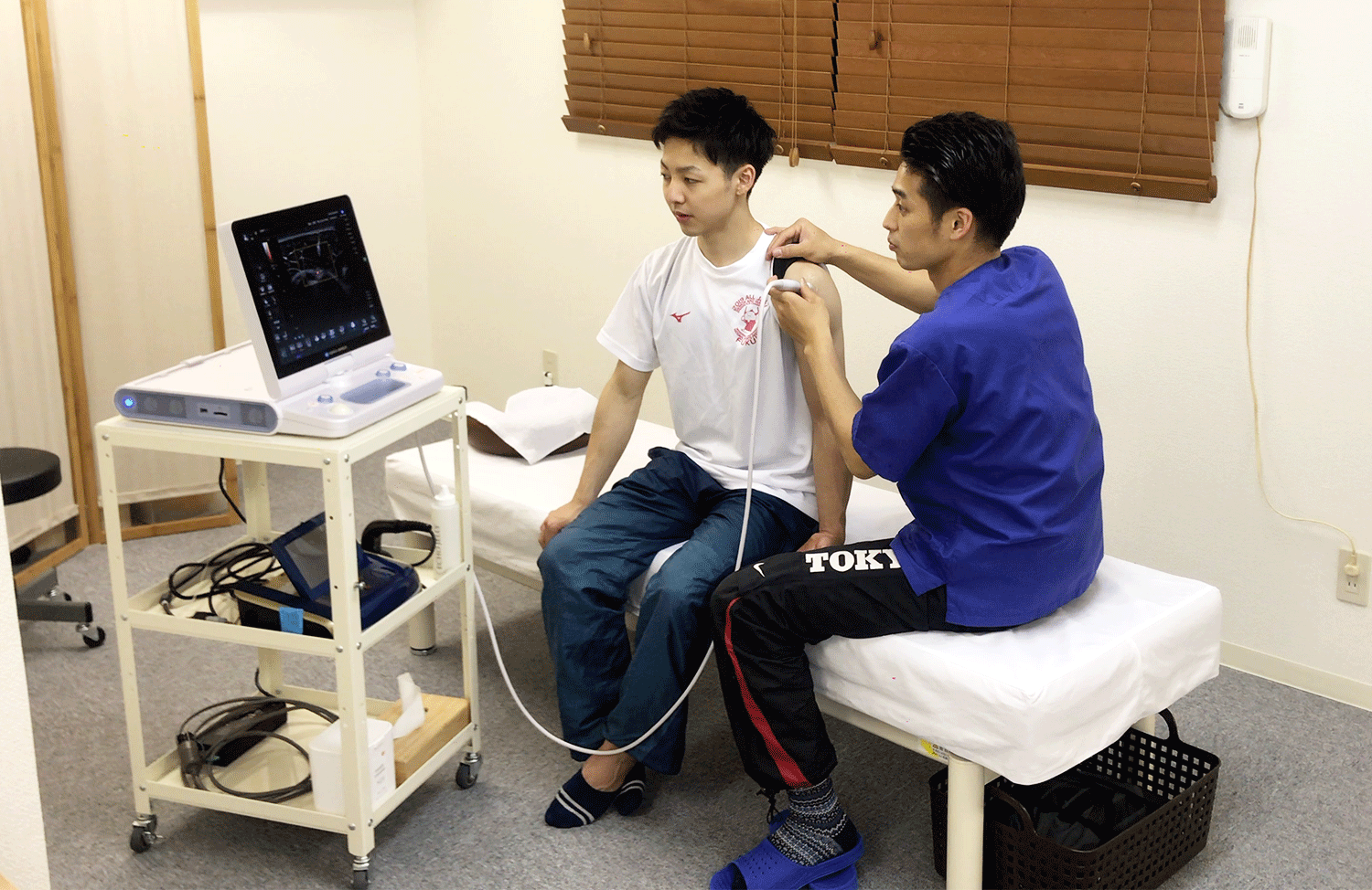 男性アスリートの肩にエコーを当てて検査する施術者